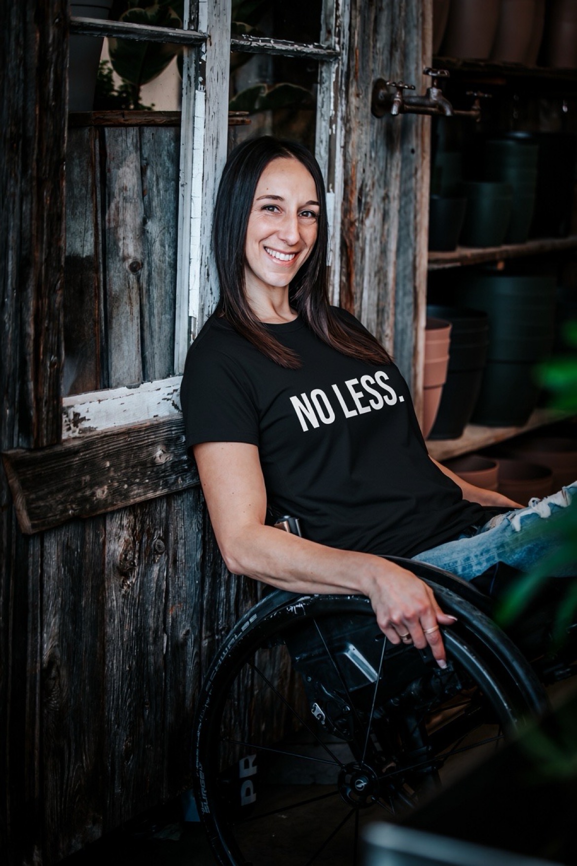 Ollie wearing the black NO LESS. t-shirt, leaning against an old wooden window
