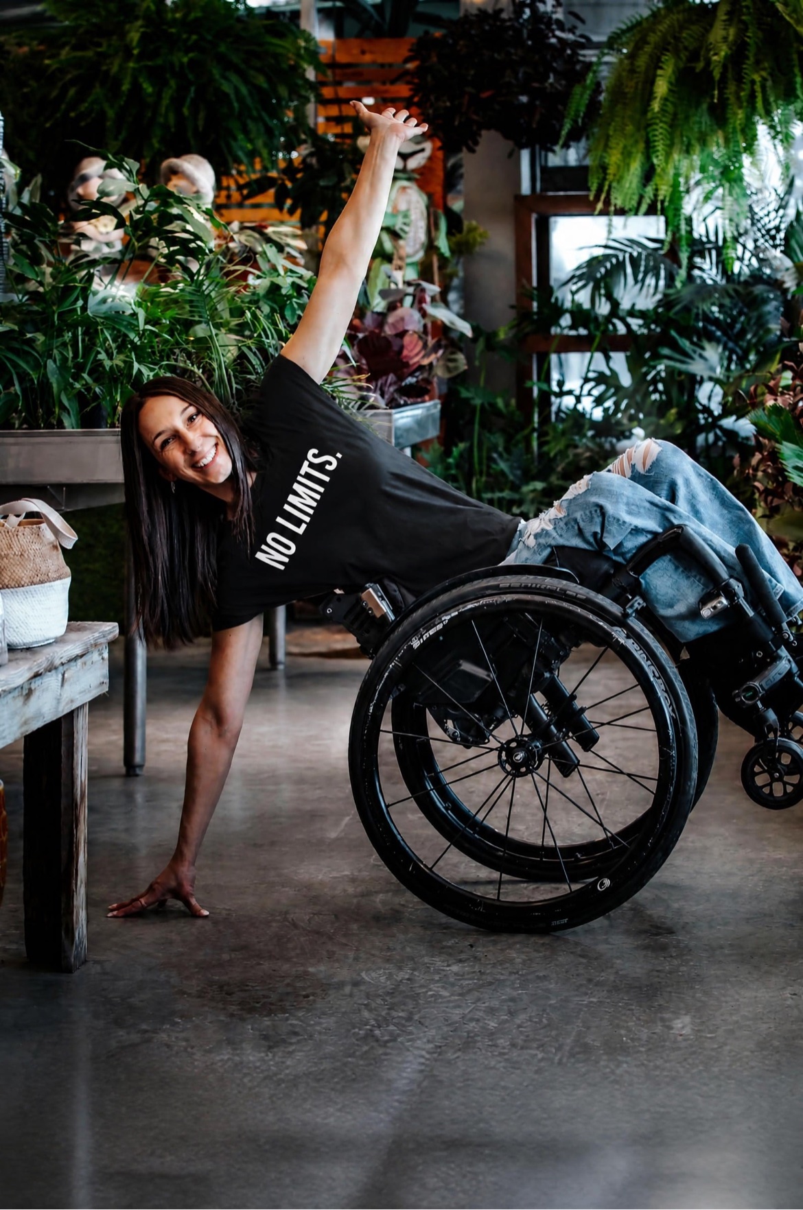 Ollie portant le t-shirt noir NO LIMITS., en wheelie dans son fauteuil roulant au milieu des plantes.